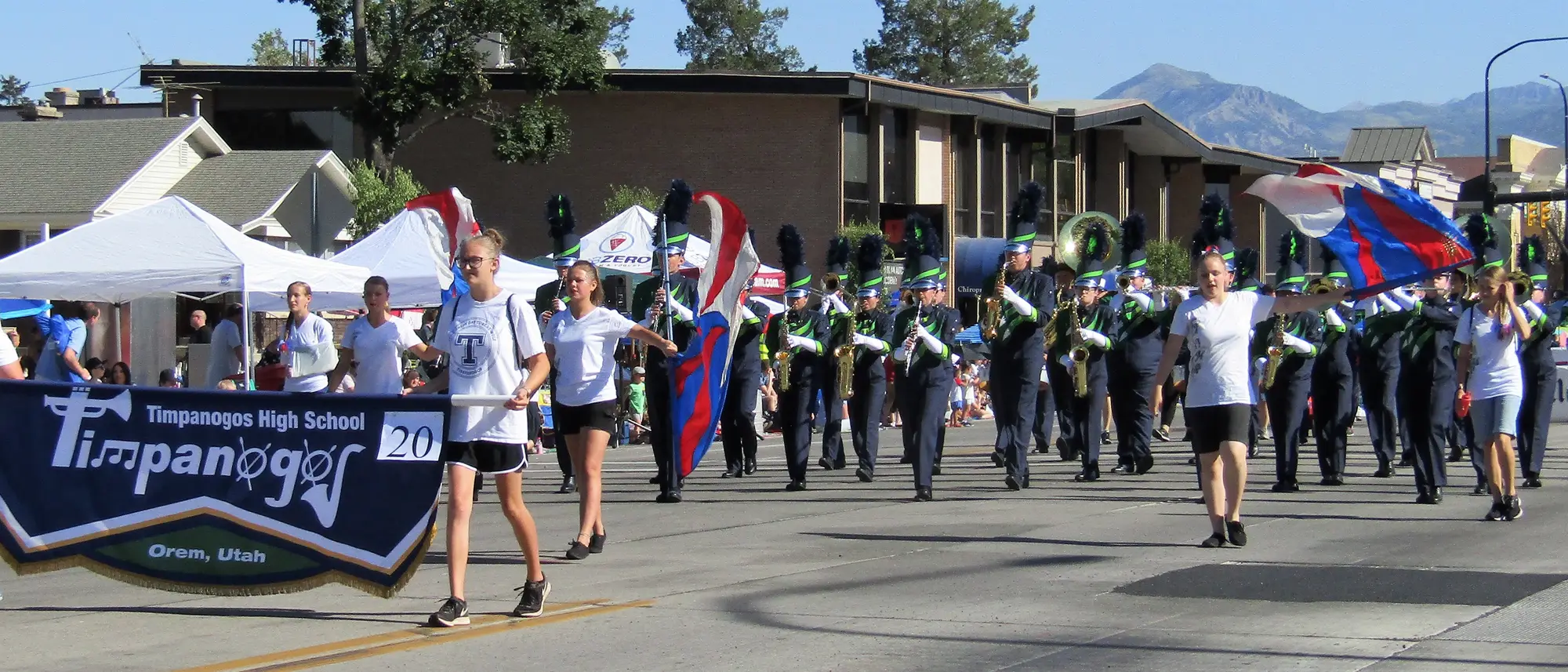 The Timpanogos High School marching band in parade formation, colour guard flags raised.